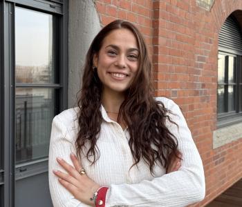 Charlotte Bootsveld in weisser Kleidung, mit langen, offenen, dunkelbraunen Haaren vor einer Backsteinwand.